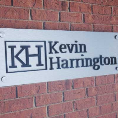 Brushed silver sign backing with black 3d letters and logo. Text reads: KH. Kevin Harrington