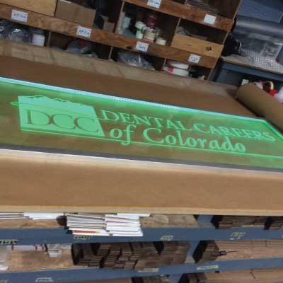 Acrylic with glowing green text and logo edge lighted indoor sign. Text reads: DCC. Dental Careers of Colorado