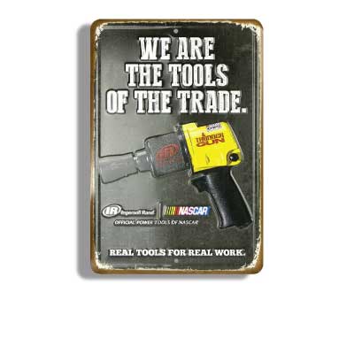 Black with rusty edges stamped metal embossed sign with picture of Nascar air ratchet gun. Text reads: We are the tools of the trade. Ingress Rand. Real tools for real work.