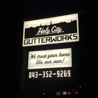 Holy City Gutterworks black and white lighted cabinet sign at night 